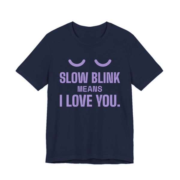 Navy t-shirt printed in lavender ink with a pair of closed cat eyes and the words “Slow Blink Means I Love You.”