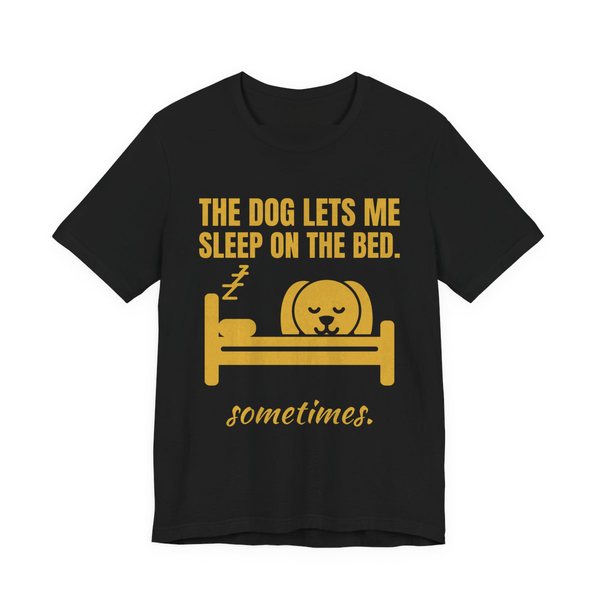 Black t-shirt printed in gold ink with a dog asleep in a bed and the words “The Dog Lets Me Sleep on the Bed. Sometimes.”