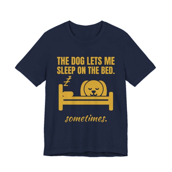 Navy t-shirt printed in gold ink with a dog asleep in a bed and the words “The Dog Lets Me Sleep on the Bed. Sometimes.”