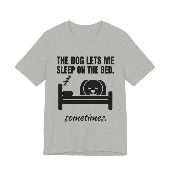 Athletic Heather t-shirt printed in dark ink with a dog asleep in a bed and the words “The Dog Lets Me Sleep on the Bed. Sometimes.”