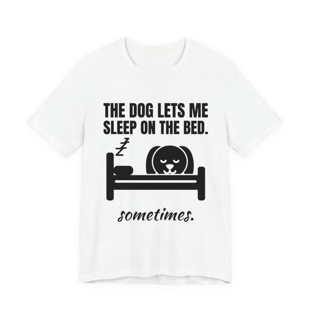White t-shirt printed in dark ink with a dog asleep in a bed and the words “The Dog Lets Me Sleep on the Bed. Sometimes.”