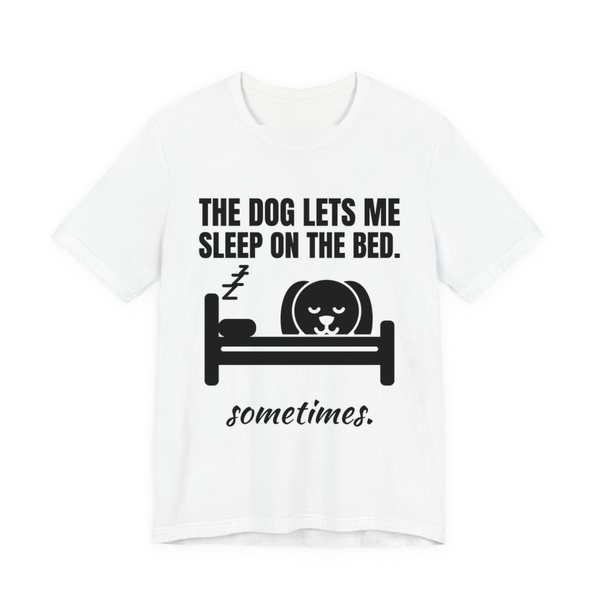White t-shirt printed in dark ink with a dog asleep in a bed and the words “The Dog Lets Me Sleep on the Bed. Sometimes.”