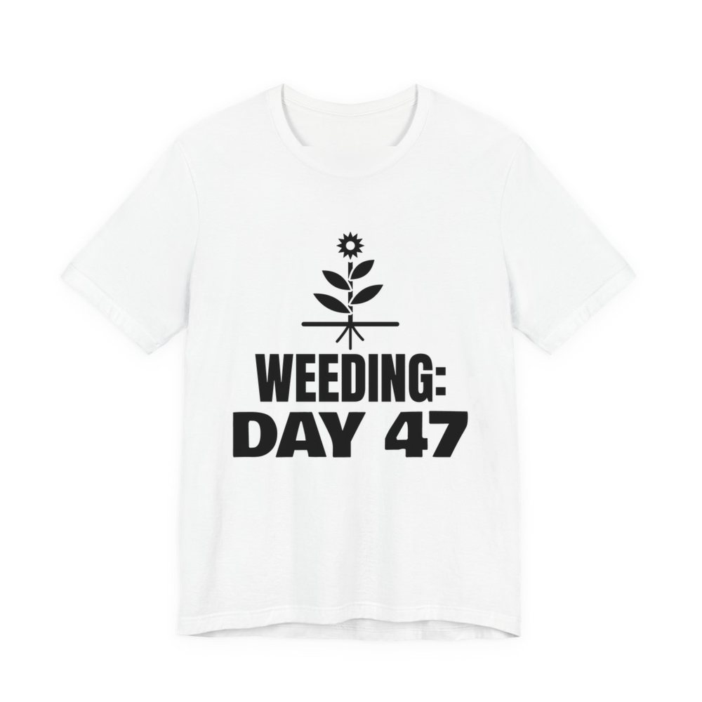 White t-shirt printed in dark ink with a flowering weed with its roots and the words “Weeding: Day 47”