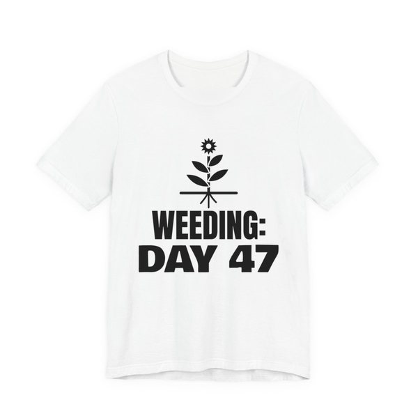 White t-shirt printed in dark ink with a flowering weed with its roots and the words “Weeding: Day 47”